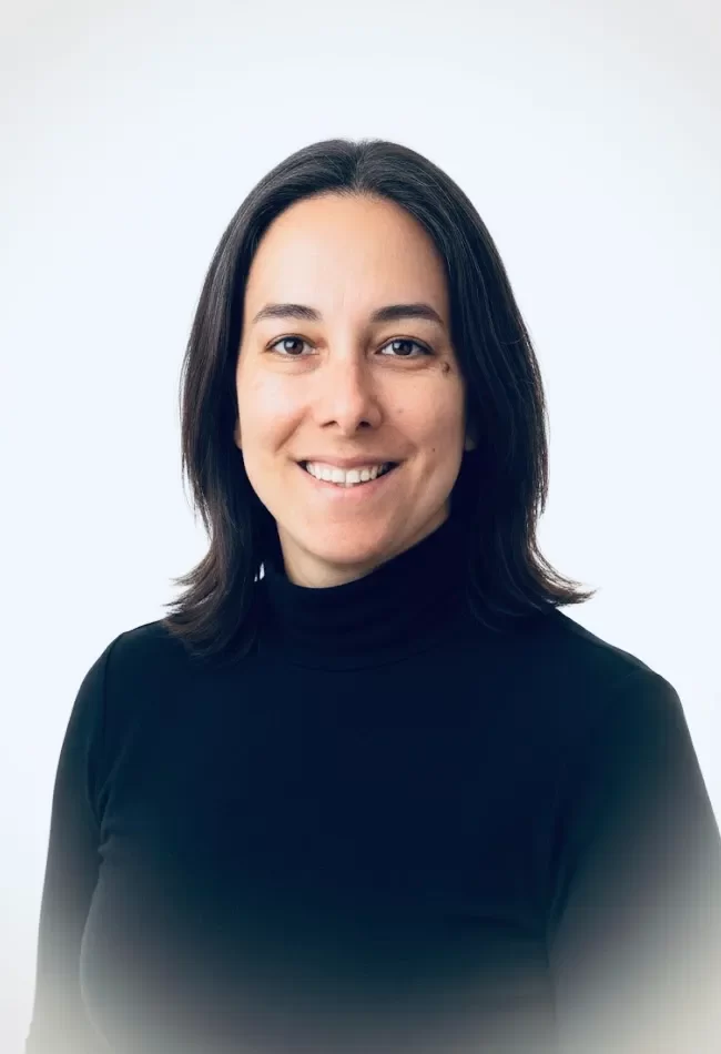 Retrato de mujer sonriendo, con cabello oscuro y suelto, vistiendo un suéter negro de cuello alto, sobre fondo claro. Ideal para representar profesionalismo y confianza.